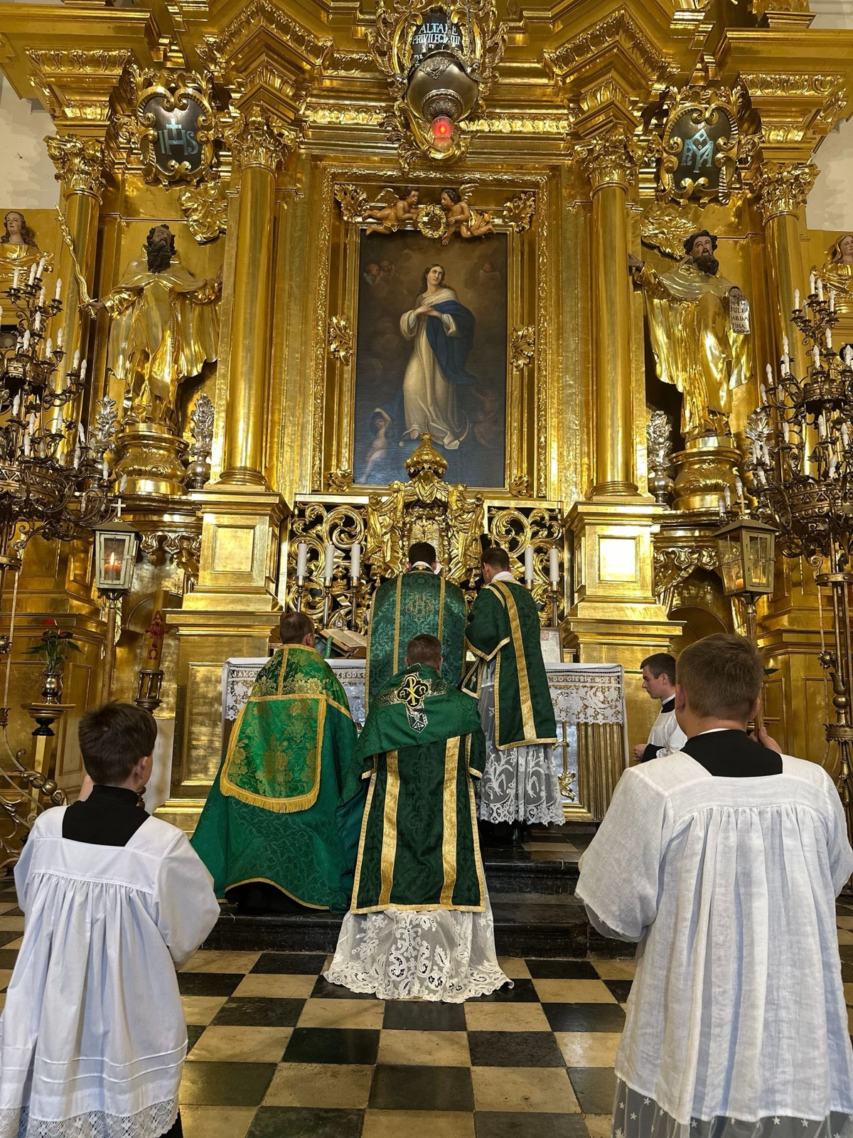 Msza święta w klasycznym rycie rzymskim przy złocistym ołtarzu — kapłani w zielonych ornatach i ministranci w komżach